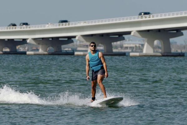 Photo of someone riding an electric surfboard around Sanibel Island with the Causeway in the background.