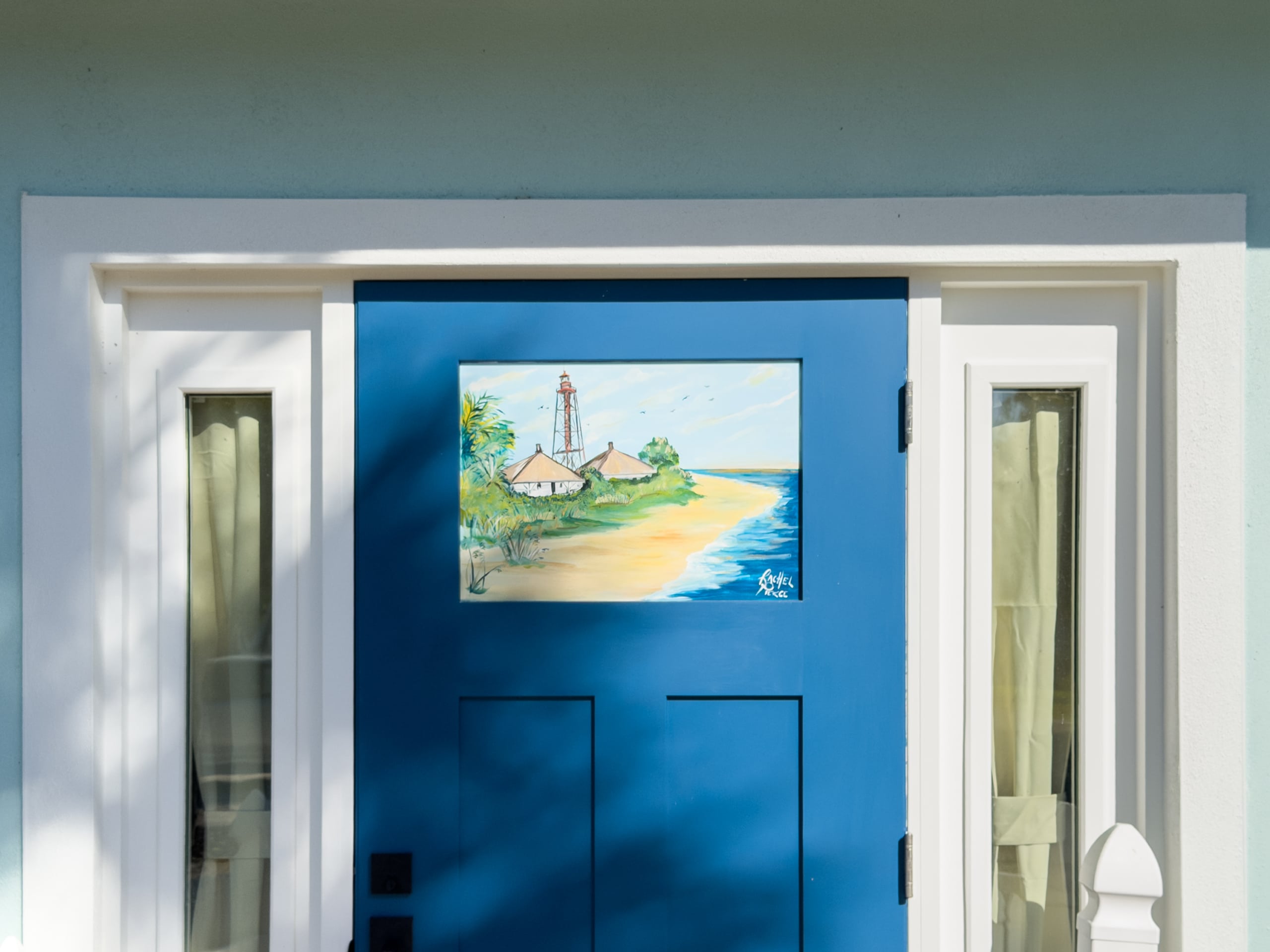 Hand-painted Sanibel Lighthouse mural by Rachel Pierce on blue cottage door at Anchor Inn & Cottages on Sanibel Island